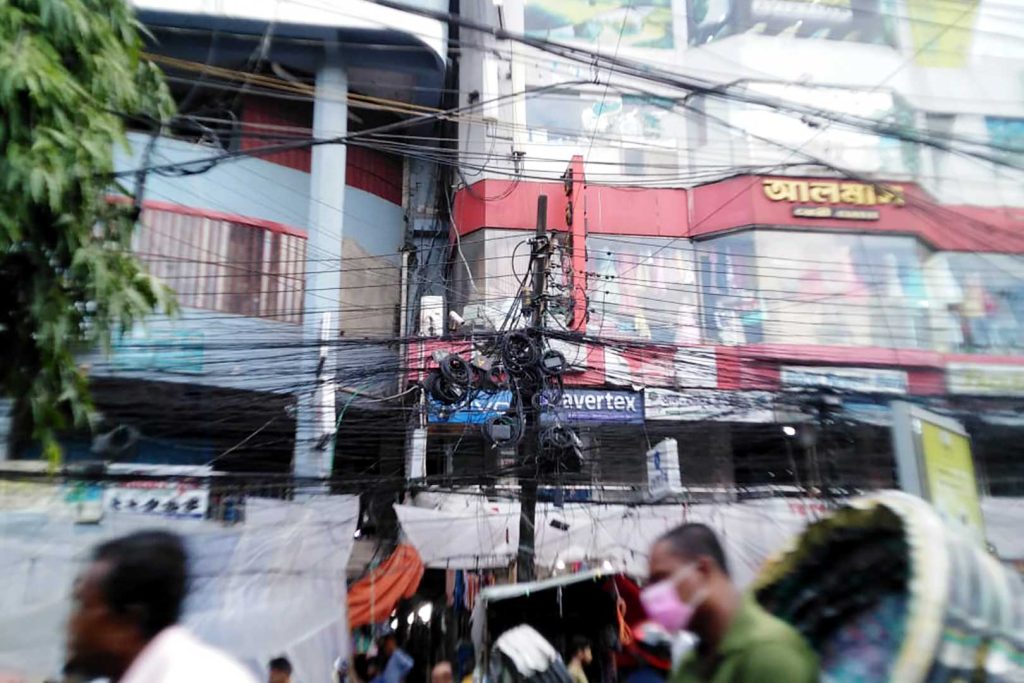 Hundred of wires tangled around telegraph pole above pavement.