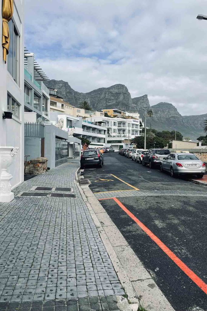 Parked cars on street in front of seaside villas with mountain range behind.