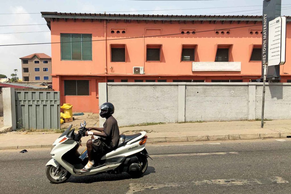 Man on motorcycle in front of salmon-pink painted building.