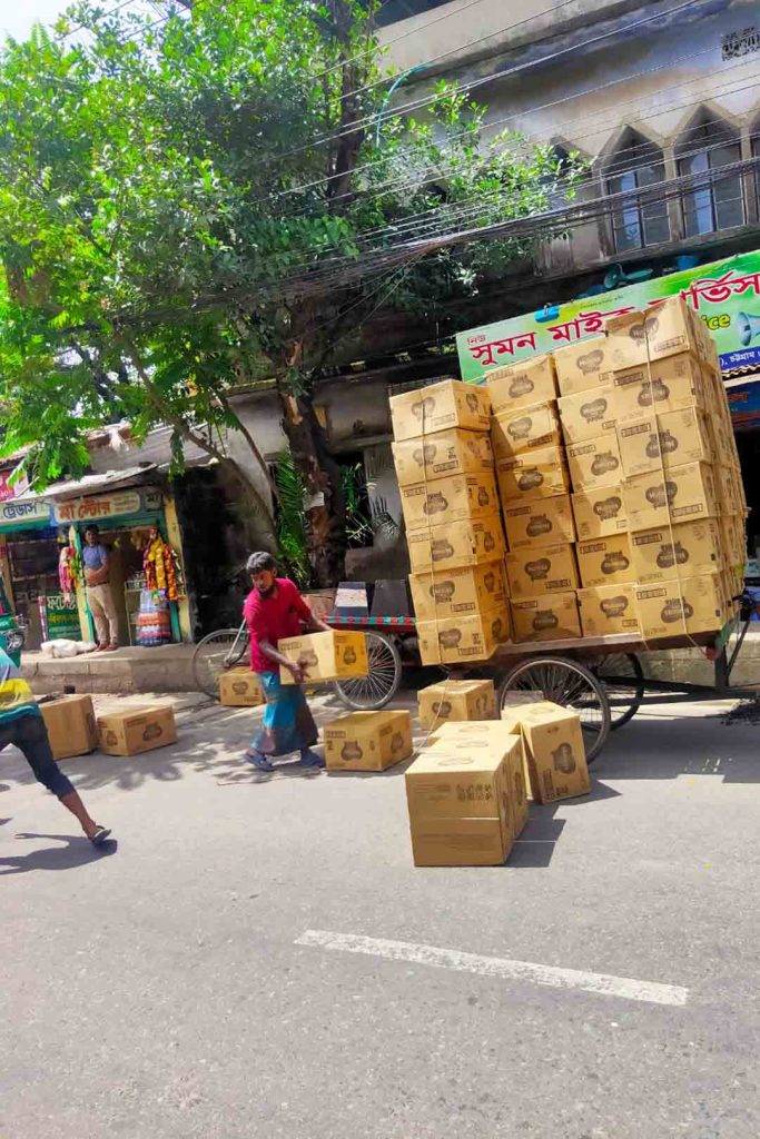 Stacks of carboard boxes tied together on cart, loose boxes on road.