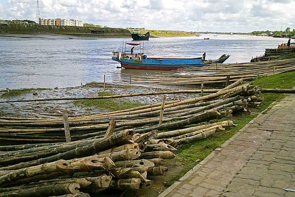 Wide river with small boat traffic, logs piled on shor ein foreground.