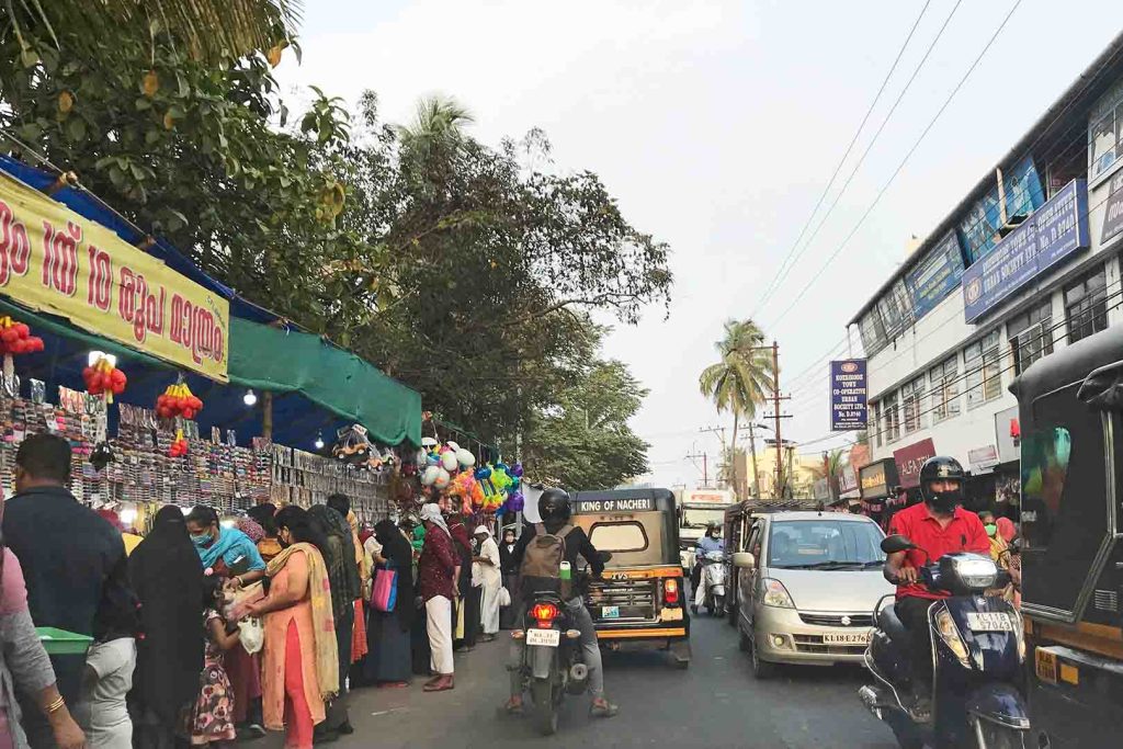 Busy road with motorcycles and cars passing pedestrians at market stalls.