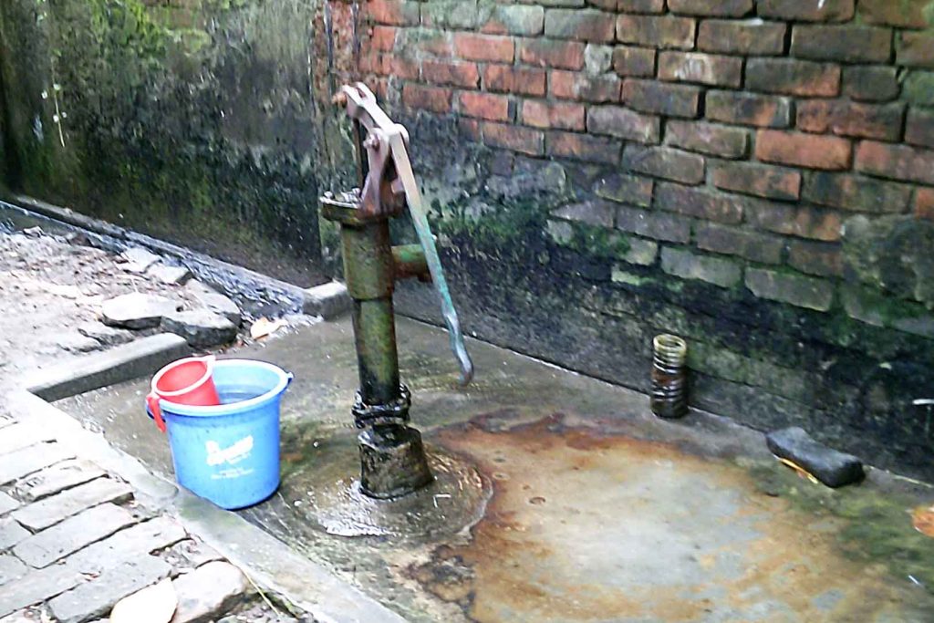 Water pump on muddy concrete base in front of brick wall.