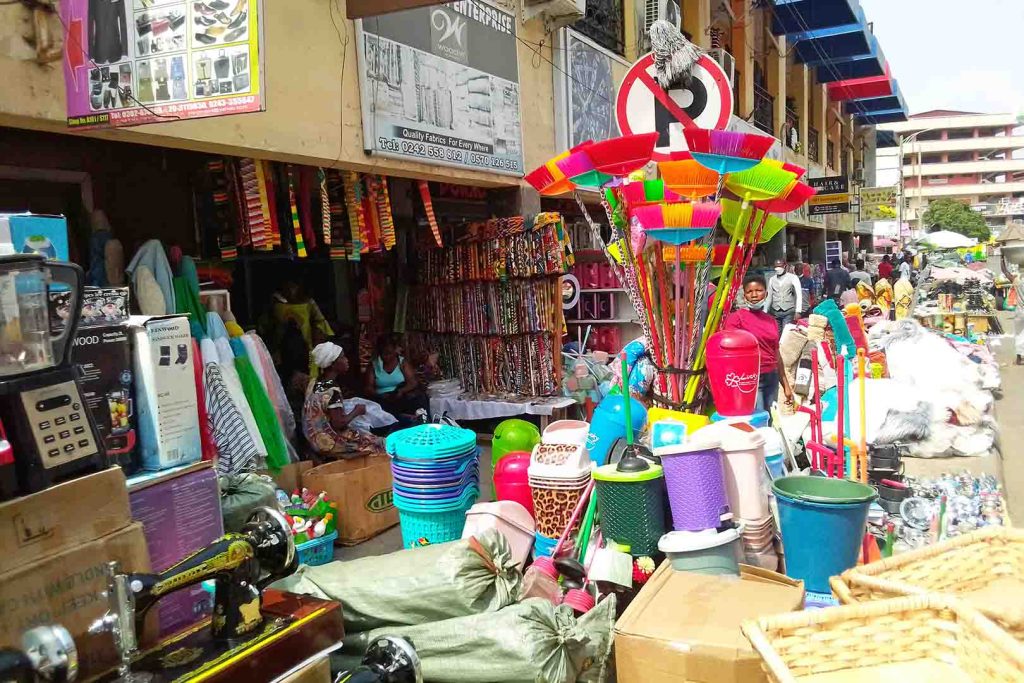 View of market stall with brightly coloured plastic containers, brushes, cardboard boxes.