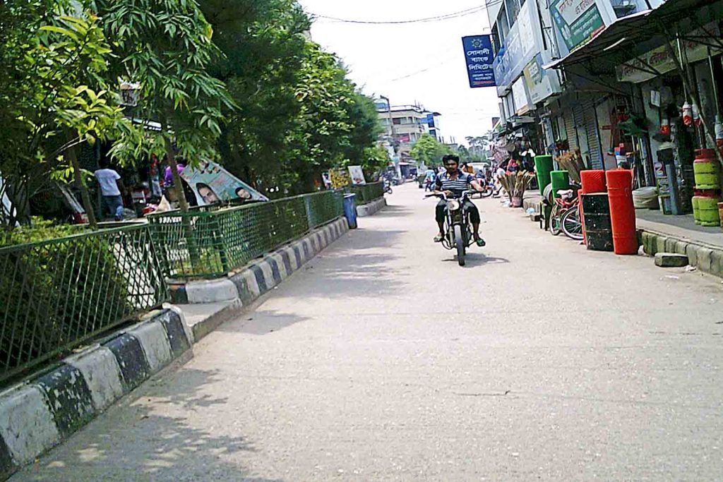 Man riding motorcycle along road lined with shops.