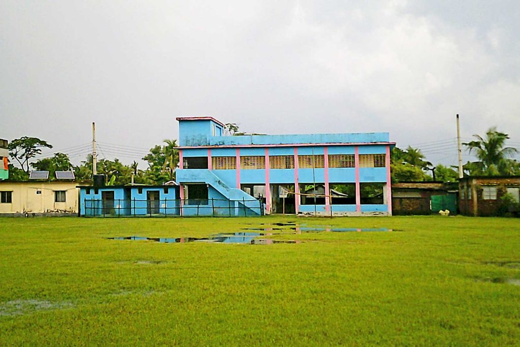 Two-storey building painted bright blue and pink in front of waterlogged field.