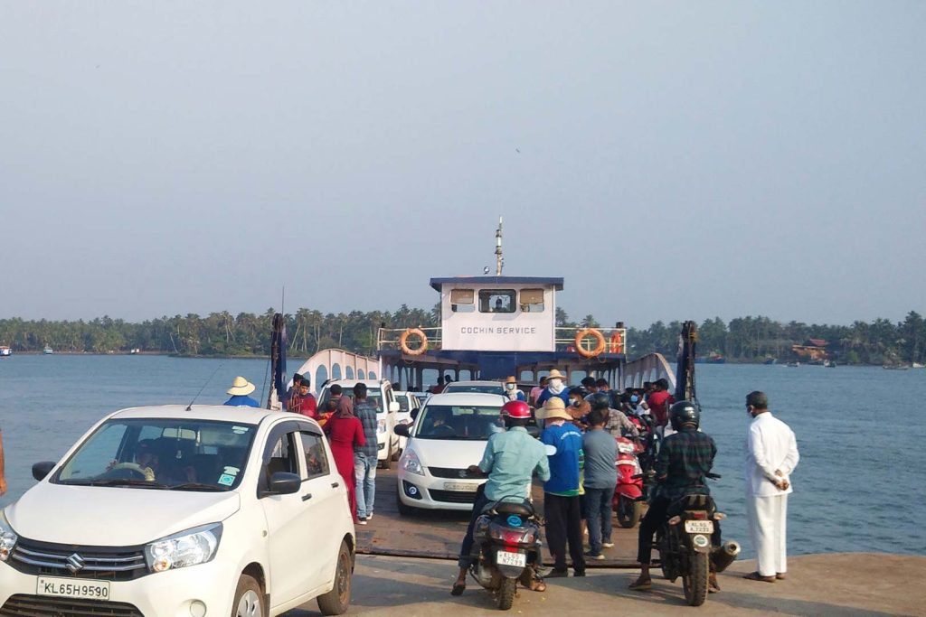 Cars disembark from a ramp at the front of a small ferry as passengers wait to board.