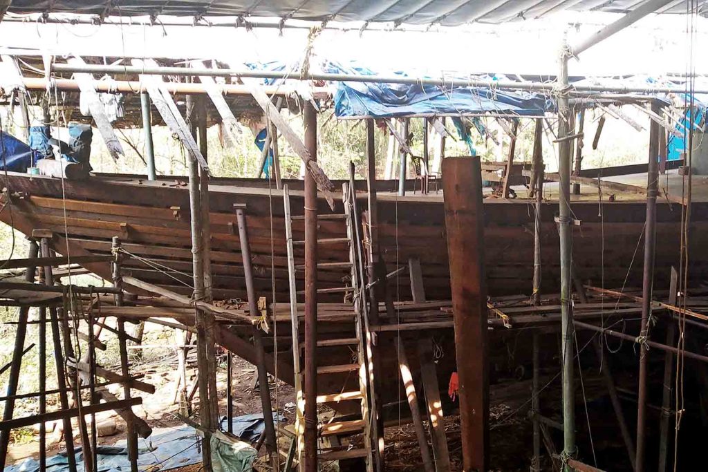 Bow of traditional timber boat under construction in open air yard.