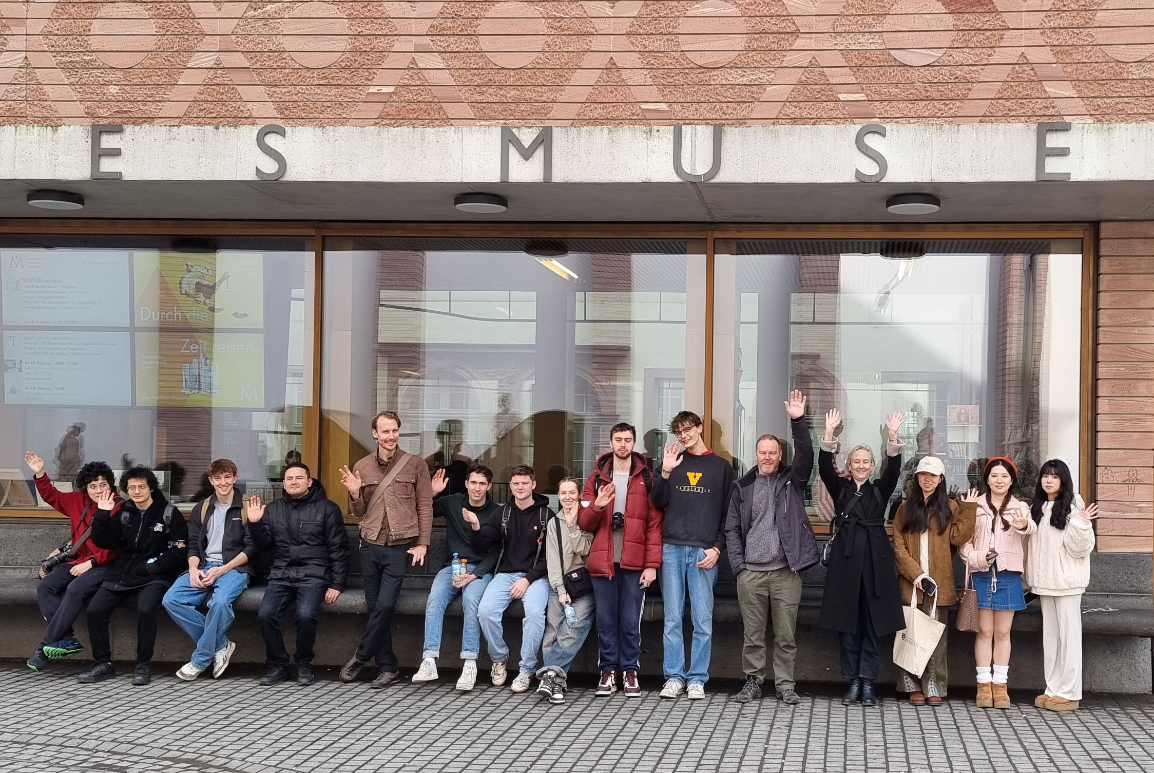 Group of students standing in front of a brick and glass facade to a building.